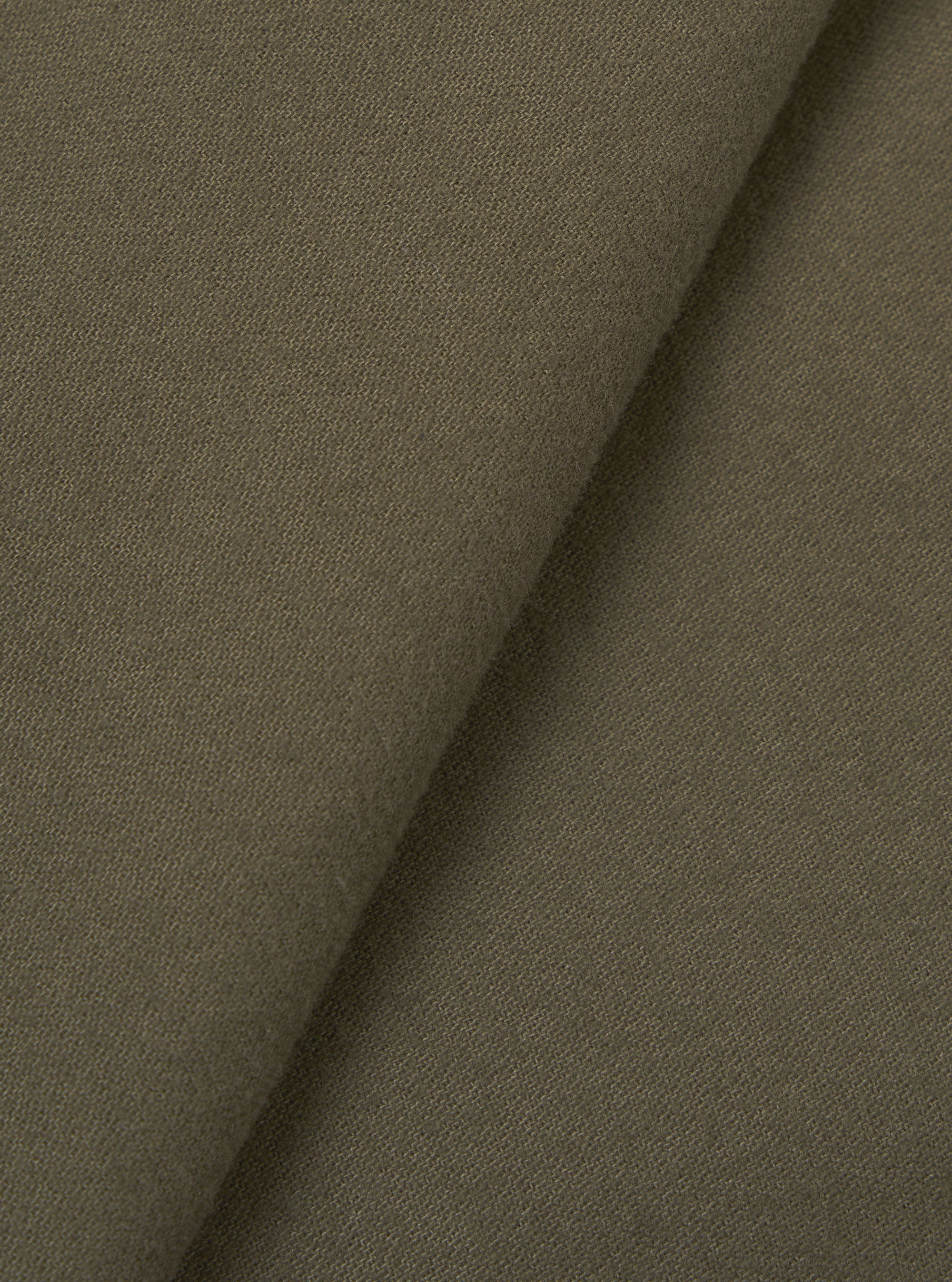 Close-up of olive brushed moleskin fabric folded diagonally, showing a fine, dense weave with a soft matte surface texture. The plain-coloured cloth has a subtle nap visible across both layers. No garment construction details are shown.