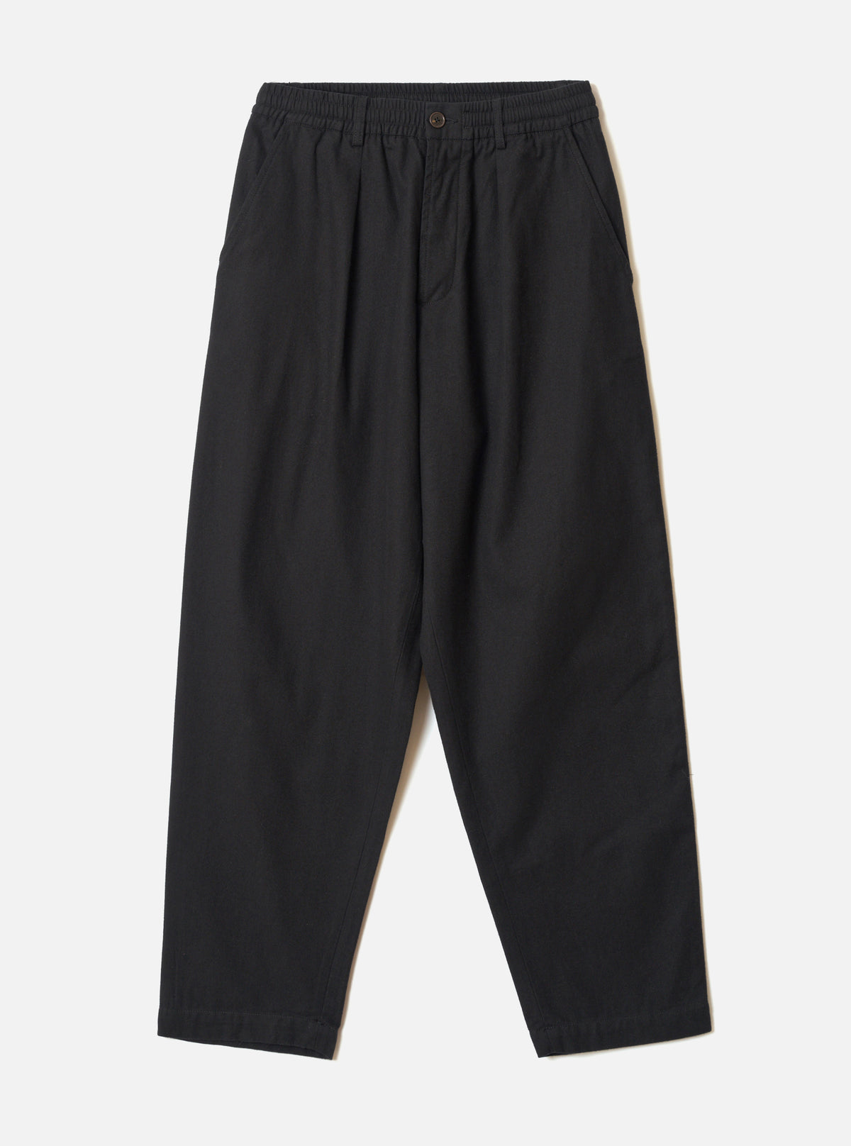Black brushed moleskin pleated track pants laid flat on a light grey seamless backdrop. The elasticated waistband features a single dark button at the centre front. Slant side pockets sit at the hips. The wide-leg silhouette tapers slightly toward the plain, unfinished hem. Fabric has a soft, matte texture throughout.