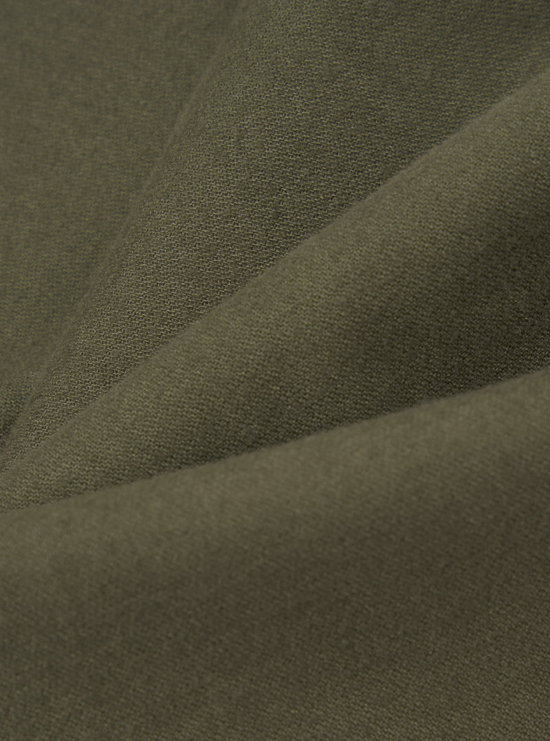 Close-up of olive brushed moleskin fabric, showing a soft, fine-knit texture with a subtle nap. The fabric is folded to reveal gentle creases and depth of colour, a muted khaki-green throughout. No garment details or background are visible.