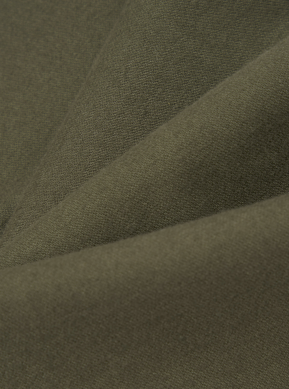 Close-up of olive brushed moleskin fabric, showing a soft, fine-knit texture with a subtle nap. The fabric is folded to reveal gentle creases and depth of colour, a muted khaki-green throughout. No garment details or background are visible.