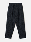 Black wool-mix track pants with an all-over abstract blurred print in dark navy and black tones. Features an elasticated waistband with a single centre button, twin pleats at the front, side slash pockets, and a relaxed tapered leg to an unfinished hem. Flat lay on a light grey studio backdrop.