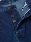 Close-up detail of the indigo work denim Dutch pant waistband and fly. Three gunmetal press-stud buttons run down the open fly placket, with the waistband folded back to reveal a light blue lining. Amber topstitching is visible throughout on the dark indigo twill fabric. Plain white studio backdrop.