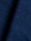 Close-up of the indigo denim fabric used in the Work Dutch Pant. The woven textile shows a fine, slightly slubby texture with tonal variation across the deep navy-indigo surface. The fabric is folded, creating a shadow crease that highlights the cloth weight and weave structure.