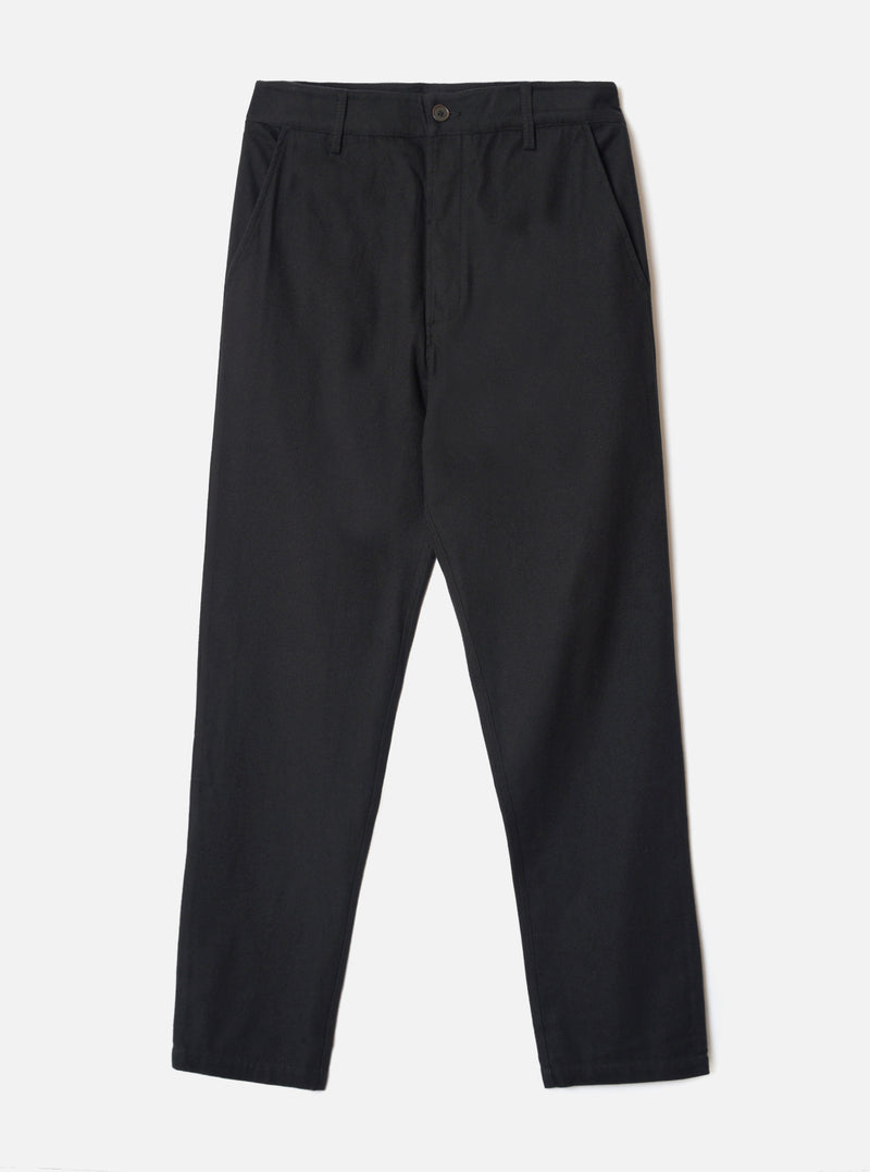 Black brushed moleskin military chinos laid flat on a light grey studio backdrop. The waistband features belt loops and a single dark button fastening at the centre front. Slant side pockets sit at the hips. The fabric has a subtle brushed texture. The trousers taper slightly from a relaxed thigh to a narrower ankle hem.