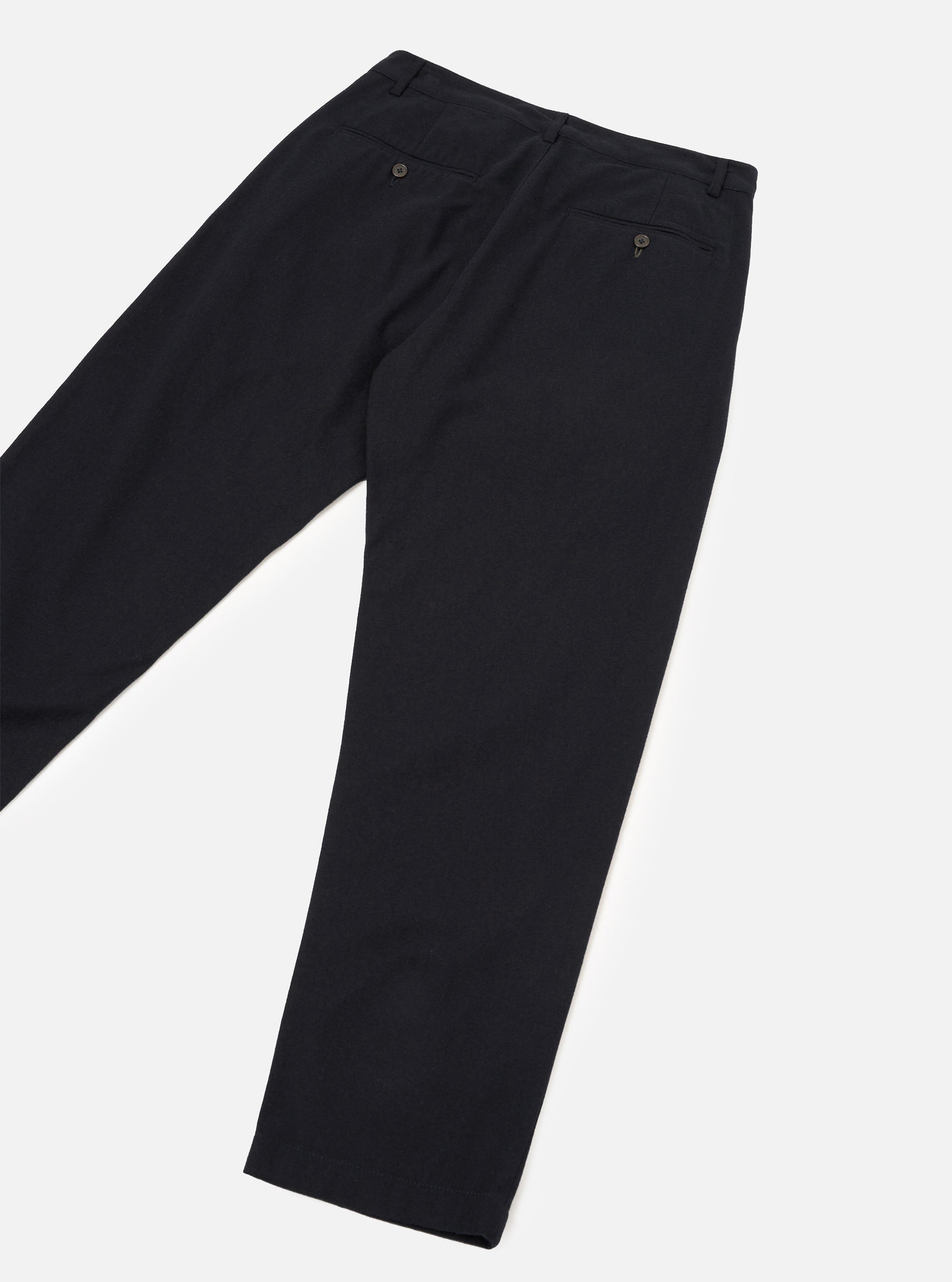 Black brushed moleskin military chino laid flat on a white studio surface, showing the back. Smooth, matte fabric with a structured waistband, belt loops, and two button-fastened welt pockets. Slim tapered leg with a clean unrolled hem. Cropped above the waistband.