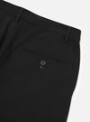 Close-up flat lay of black brushed moleskin military chinos on a white studio surface, showing the rear waistband with two belt loops, a single welt back pocket fastened with a dark four-hole button and contrast bartack stitching. The fabric has a smooth, fine-brushed texture.