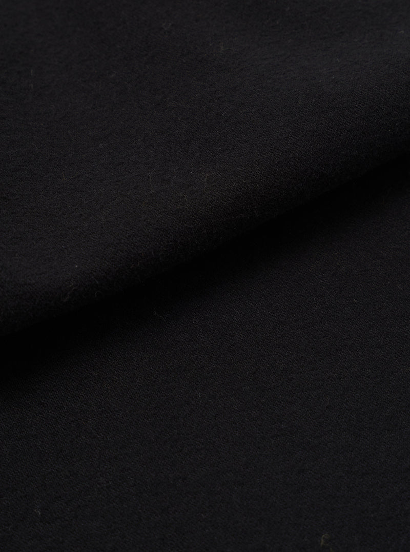 Close-up of black brushed moleskin fabric, showing a dense, soft-napped texture with gentle folds creating subtle shadow and depth across the surface.