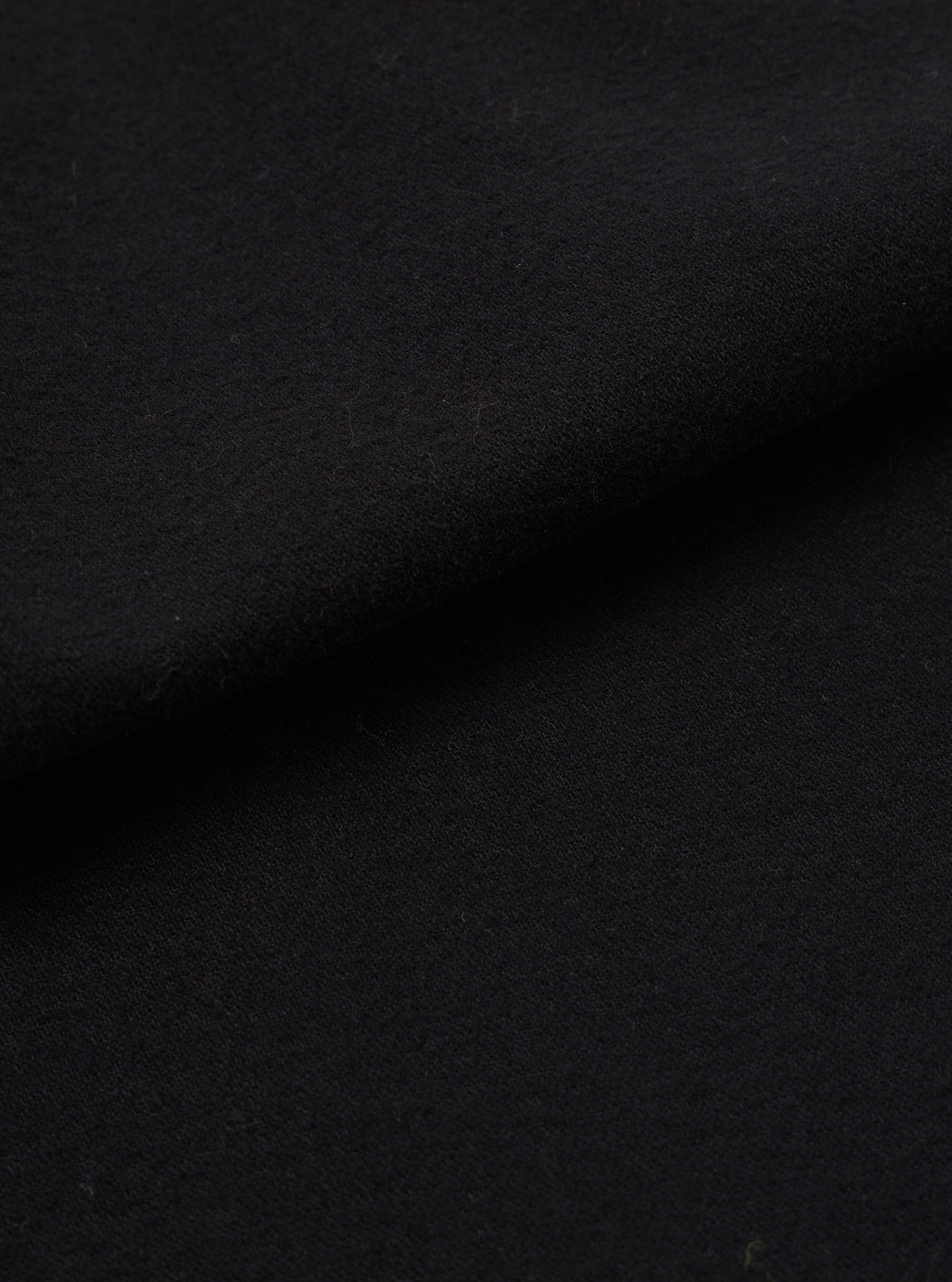 Close-up of black brushed moleskin fabric, showing a dense, soft-napped texture with gentle folds creating subtle shadow and depth across the surface.