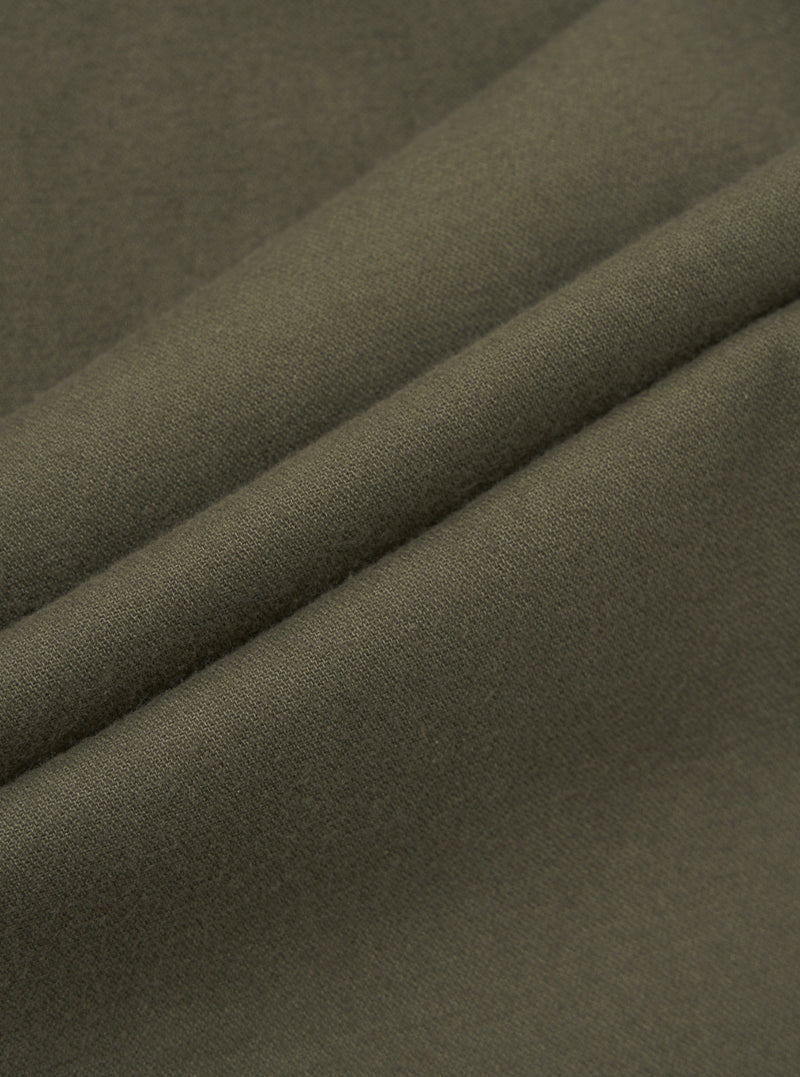 Close-up of olive brushed moleskin fabric, showing a soft, fine-textured surface with a subtle matte finish. The cloth is folded to reveal two raised ridges, highlighting the fabric weight and smooth hand-feel. The solid khaki-green tone is consistent throughout, with no pattern or sheen visible.
