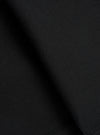 Close-up fabric detail of black brushed moleskin trousers, showing the dense, soft-napped texture of the cloth. The tight knit weave is visible in the upper corner, contrasting with the smooth brushed surface. Deep folds create areas of shadow across the matte black fabric.