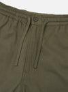 Close-up of the waistband on olive brushed moleskin hi water trousers. The elasticated waistband features a matching fabric-covered section, a dark four-hole button, and a woven drawcord threaded through two eyelets hanging loose. Plain white studio backdrop.