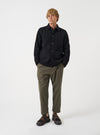 A model wearing the Universal Works Olive Brushed Moleskin Hi Water Trouser, captured from the front against a plain backdrop. The cropped olive green trousers show an adjustable drawstring waist, slant pockets, and a slim tapered cut.
