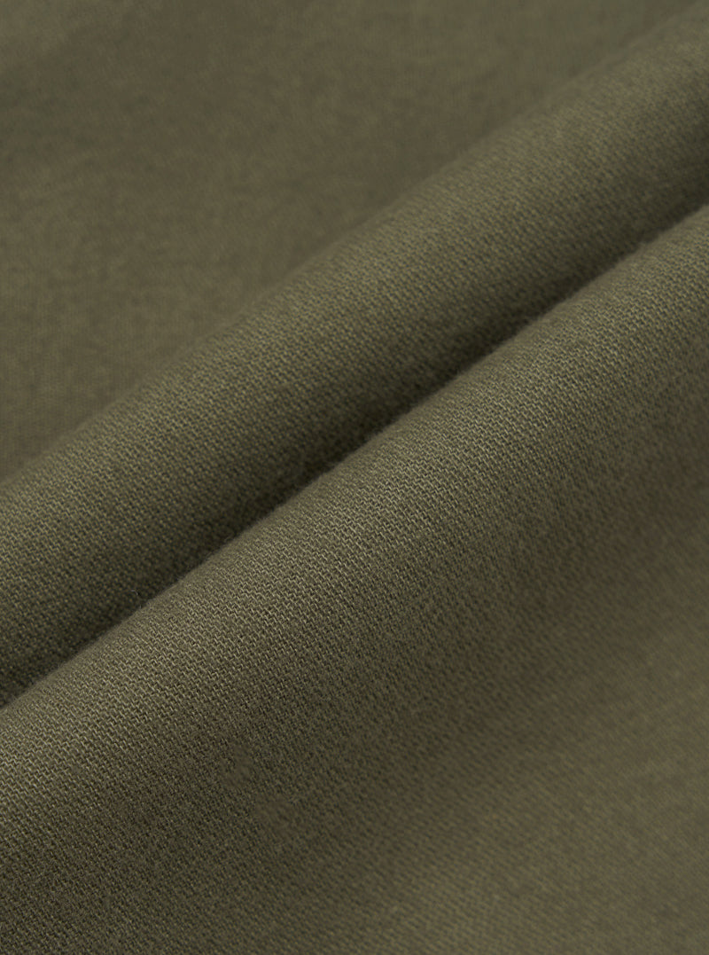 Close-up detail shot of olive brushed moleskin fabric, showing a folded edge that highlights the fine knit texture and soft surface finish. The solid, muted khaki-green cloth has a dense, smooth hand visible across the fold. No background is visible.
