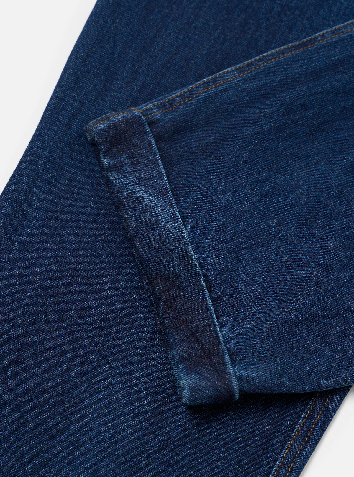 Close-up flat lay of the indigo work denim super chino on a white surface, showing the crotch and thigh area in dark indigo twill denim with amber topstitching. The fly seam and coin pocket seam are visible, highlighting the fabric's tight weave and structured construction.