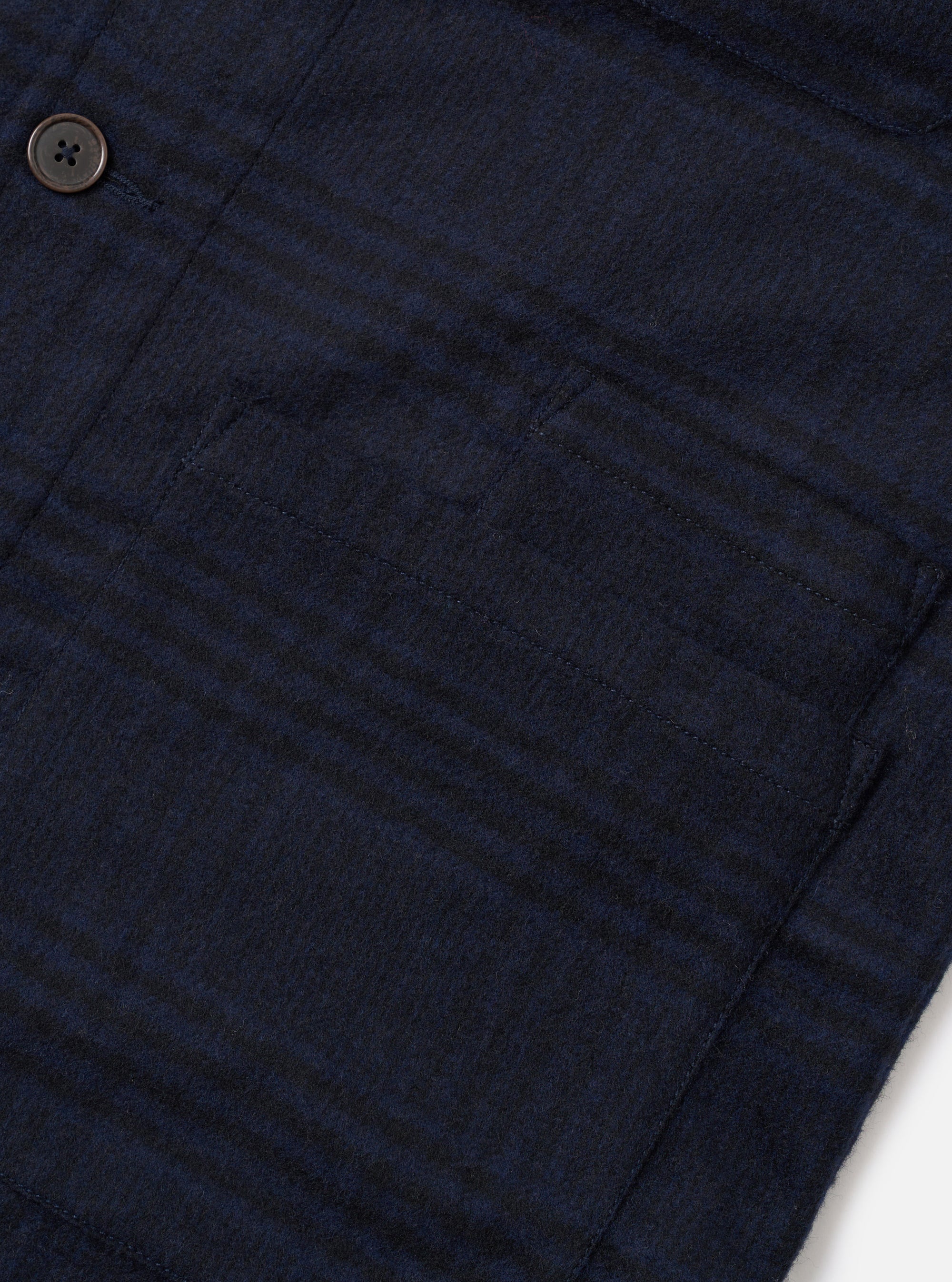 Close-up flat lay of the navy Bob Wool Mix Bakers Overshirt on a white surface, showing a large patch chest pocket with topstitched edges and a dark horn-effect button above. The fabric has a brushed wool-mix texture with a subtle dark navy check pattern.