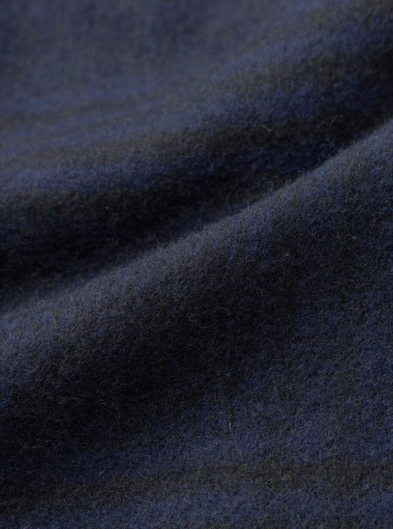 Close-up of the navy wool mix fabric used in the Kyoto Work Jacket. The brushed, softly felted surface shows fine individual fibres and a subtle dark mélange tone. Gentle folds across the cloth highlight its weight and texture.