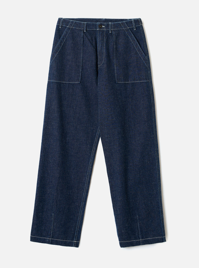 Indigo denim fatigue trousers laid flat on a light grey seamless backdrop. Wide-leg cut in raw indigo denim with visible white contrast topstitching throughout. Structured waistband with a single button fastening and no belt loops. Two large square patch pockets sit on the front thighs. Angled side seams and vent slits at the hem.