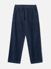Indigo denim fatigue trousers laid flat on a light grey seamless backdrop. Wide-leg cut in raw indigo denim with visible white contrast topstitching throughout. Structured waistband with a single button fastening and no belt loops. Two large square patch pockets sit on the front thighs. Angled side seams and vent slits at the hem.