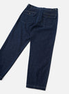 Indigo denim fatigue trousers laid flat on a light grey surface, showing the rear. Two large flap patch pockets sit at the back waist, each with a brass button closure. Contrast white topstitching runs throughout. The waistband features additional brass hardware at the sides. Wide-leg silhouette tapers slightly to a cuffed hem.