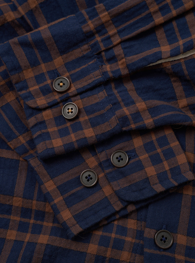 A detailed studio shot of the Navy/Brown Young Check CPO Shirt against a plain backdrop. The close-up emphasizes the fabric's woven texture, button detailing, and neat chest pocket stitching.