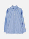 Blue and white vertical stripe long-sleeve shirt laid flat on a light grey studio backdrop. Features a point collar, central button placket with white buttons, a single patch chest pocket, and buttoned barrel cuffs. A Universal Works woven label is visible at the neck. Smooth cotton fabric with a crisp finish.