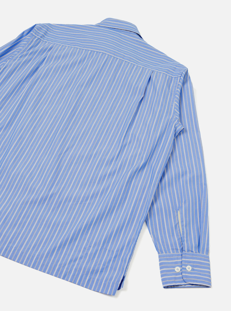 Blue and white pinstripe compact cotton shirt shot from above as a flat lay on a light grey surface, showing the back and one sleeve. A back yoke seam sits below the collar. The long sleeve ends in a buttoned cuff with two white buttons. A side hem vent is visible at the bottom.