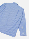 Blue and white pinstripe compact cotton shirt shot from above as a flat lay on a light grey surface, showing the back and one sleeve. A back yoke seam sits below the collar. The long sleeve ends in a buttoned cuff with two white buttons. A side hem vent is visible at the bottom.