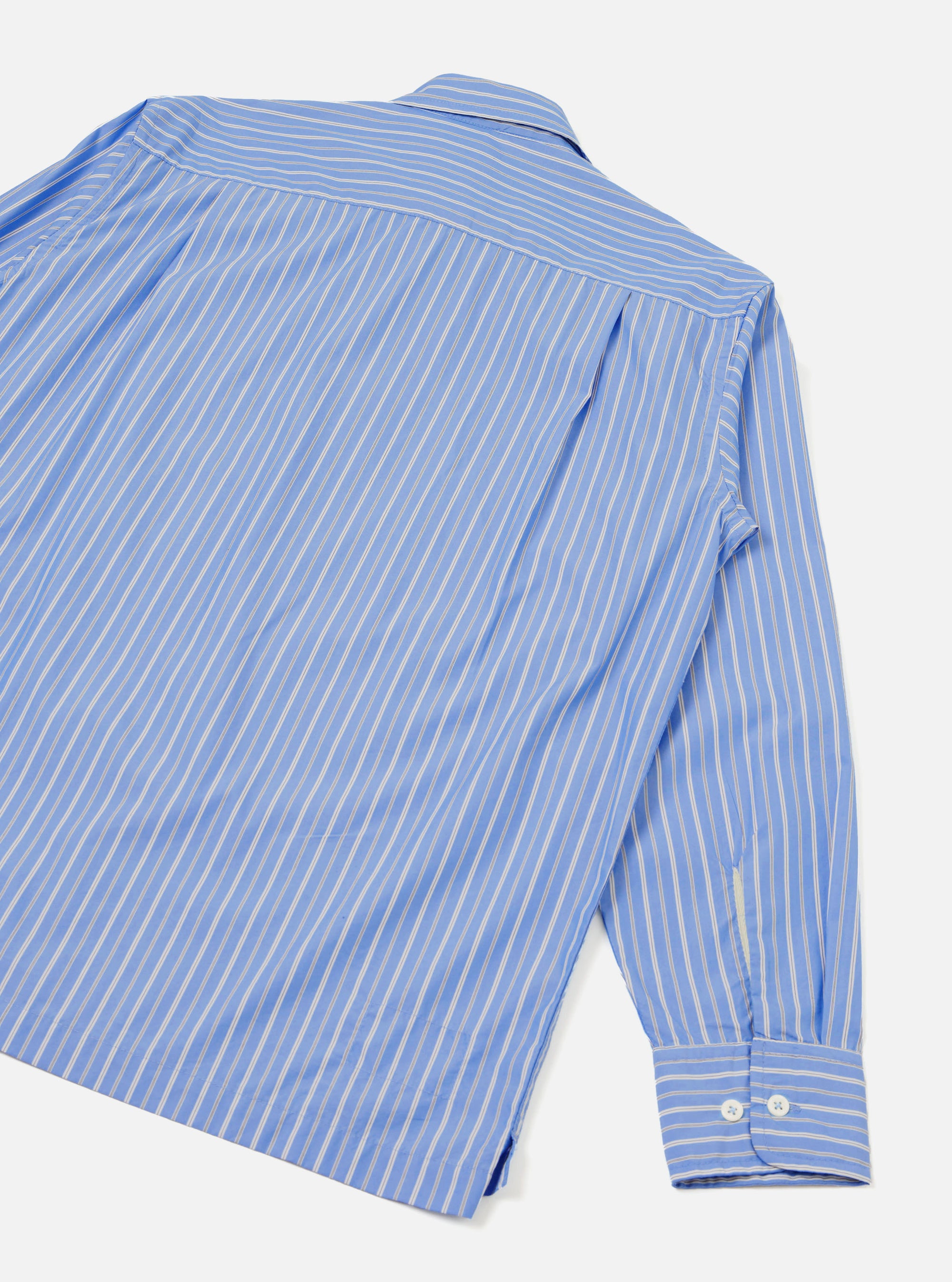 Blue and white pinstripe compact cotton shirt shot from above as a flat lay on a light grey surface, showing the back and one sleeve. A back yoke seam sits below the collar. The long sleeve ends in a buttoned cuff with two white buttons. A side hem vent is visible at the bottom.