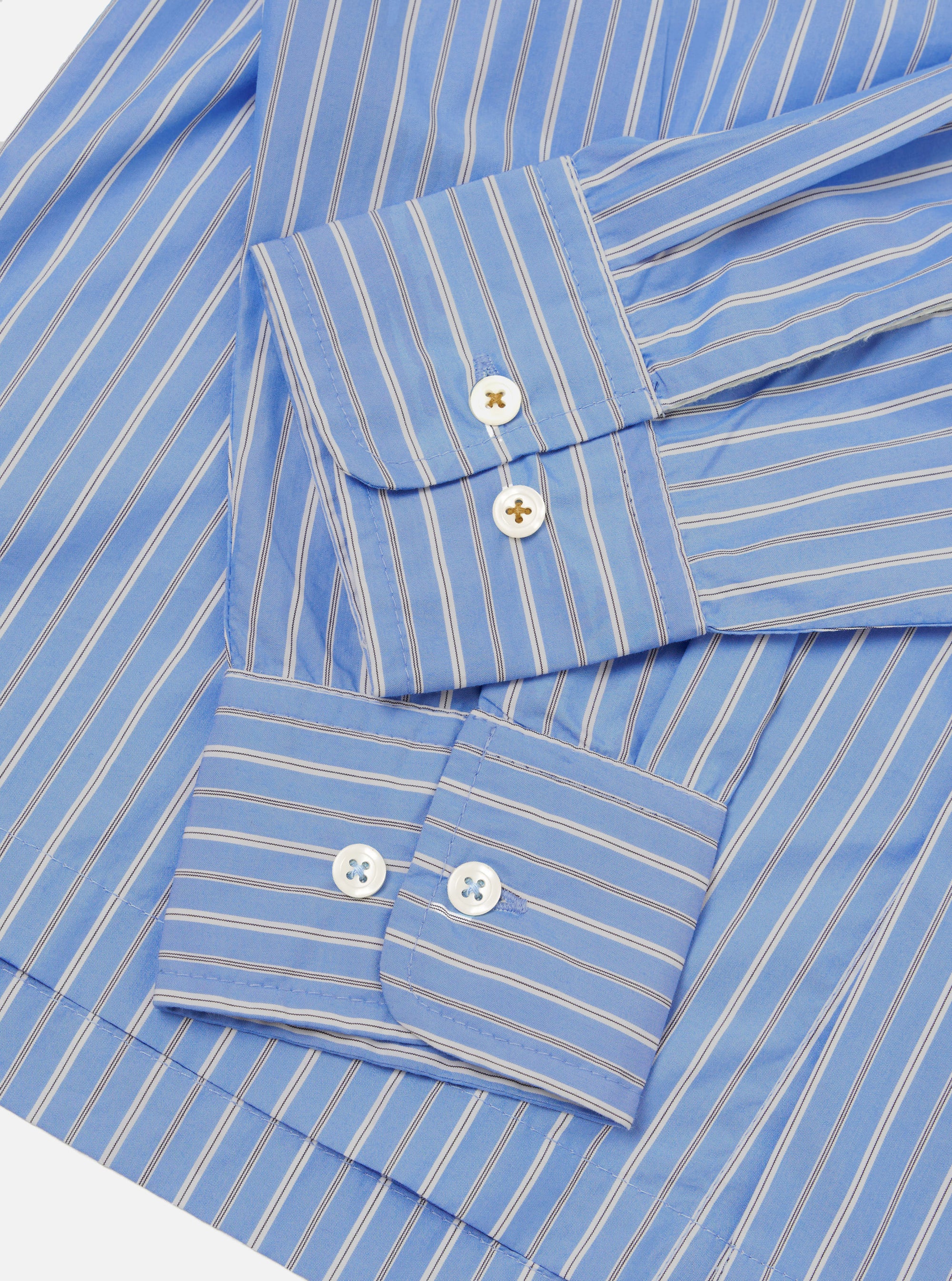 Close-up flat lay of the blue stripe Refab compact cotton Lucky shirt, focusing on both cuffs. The smooth cotton fabric features narrow dark and white stripes on a blue ground. Each double-button barrel cuff shows two white mother-of-pearl buttons. Shot on a white studio backdrop.
