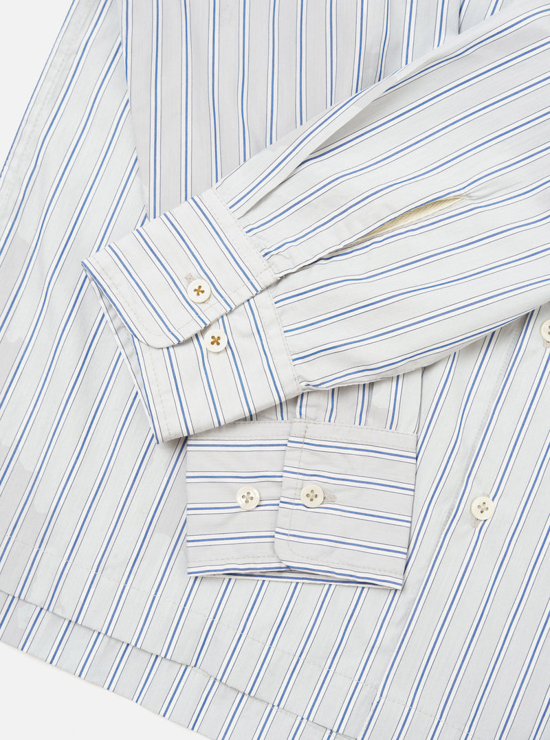 Flat lay close-up of the grey striped Lucky Shirt on a white surface, focusing on the cuffs and lower sleeves. The compact cotton fabric features blue and navy vertical stripes on a light grey ground. Both barrel cuffs are unfolded and fastened with two cream four-hole buttons each.