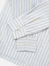 Flat lay close-up of the grey striped Lucky Shirt on a white surface, focusing on the cuffs and lower sleeves. The compact cotton fabric features blue and navy vertical stripes on a light grey ground. Both barrel cuffs are unfolded and fastened with two cream four-hole buttons each.