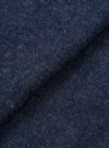 Close-up of the indigo denim fabric used in the OG Bakers Chore Jacket. The textured weave shows a deep navy-blue base with flecks of white and cream throughout, giving a slubby, neppy character. The fabric is folded, creating a diagonal crease across the frame.