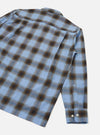 Blue check long-sleeve shirt in a soft ombre plaid with brown and dark navy tones on a light blue ground. Shot flat on a white studio backdrop, angled to show the back and one sleeve. A camp collar is visible at the top. The cuff features two white buttons and a gauntlet placket.