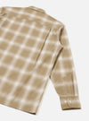 Flat lay of a sand check long-sleeve shirt on a light grey studio surface, shot from behind at an angle. The back panel and one full sleeve are visible, showing a soft ombre check pattern in sand and white on a smooth, slightly lustrous fabric. The cuff fastens with two small buttons.