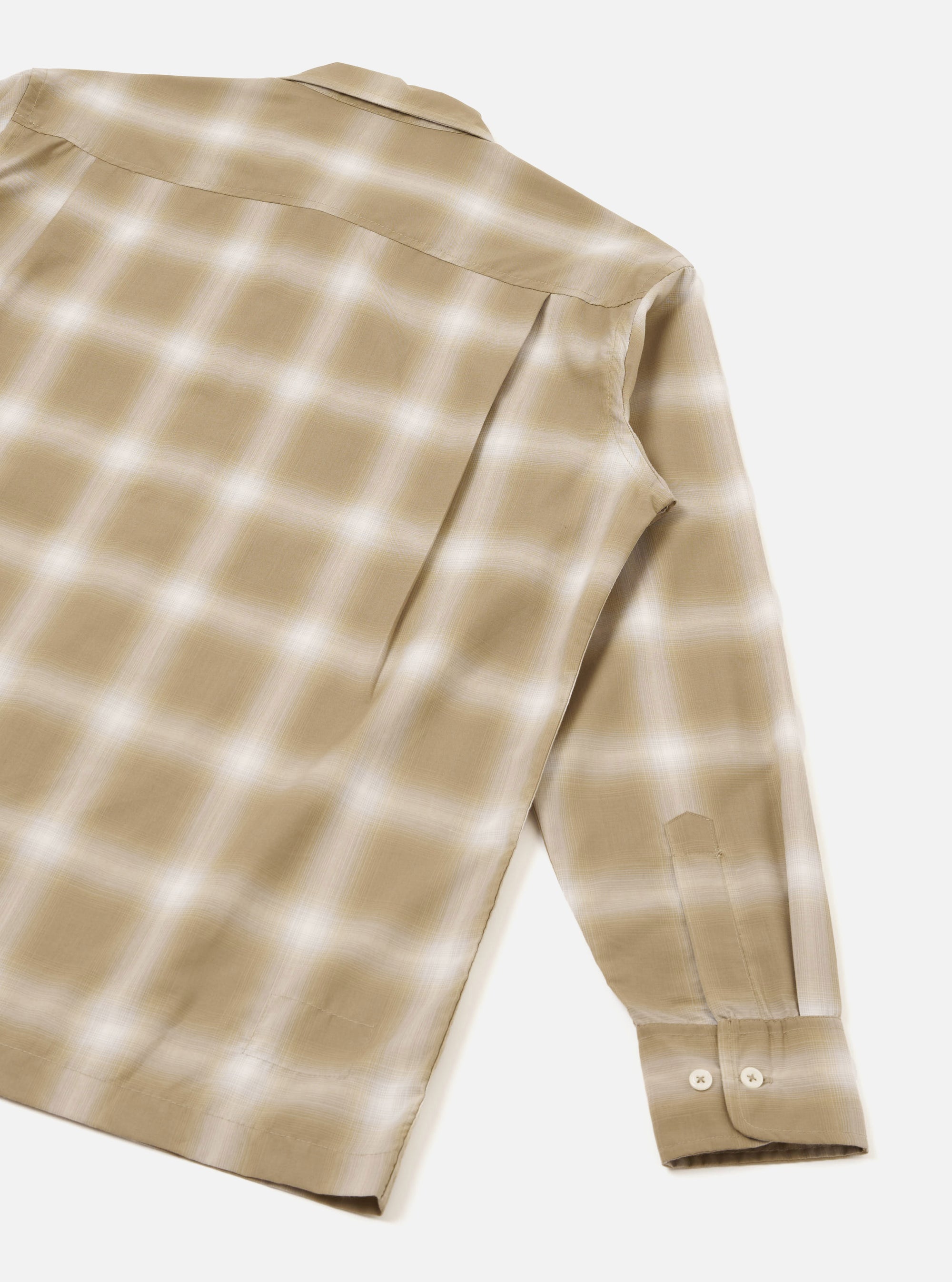 Flat lay of a sand check long-sleeve shirt on a light grey studio surface, shot from behind at an angle. The back panel and one full sleeve are visible, showing a soft ombre check pattern in sand and white on a smooth, slightly lustrous fabric. The cuff fastens with two small buttons.