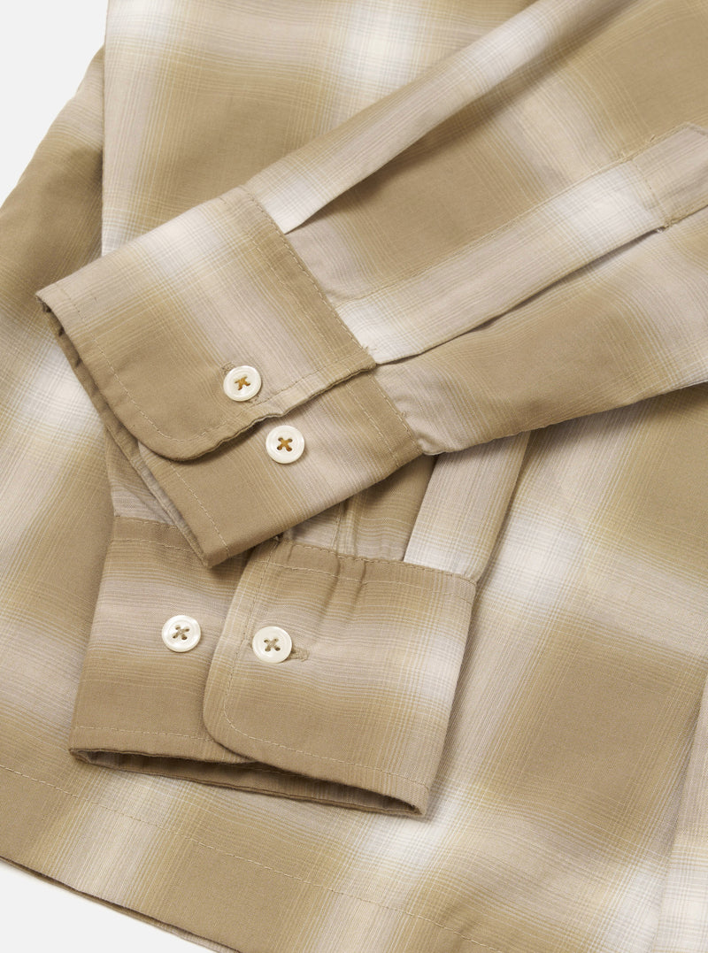 Flat lay close-up of the sand check shirt's cuffs and sleeves on a white surface. The fabric features a tonal ombre check pattern in beige, sand and cream. Both buttoned barrel cuffs are visible, each fastened with two cream four-hole buttons. The lightweight woven fabric has a subtle sheen.