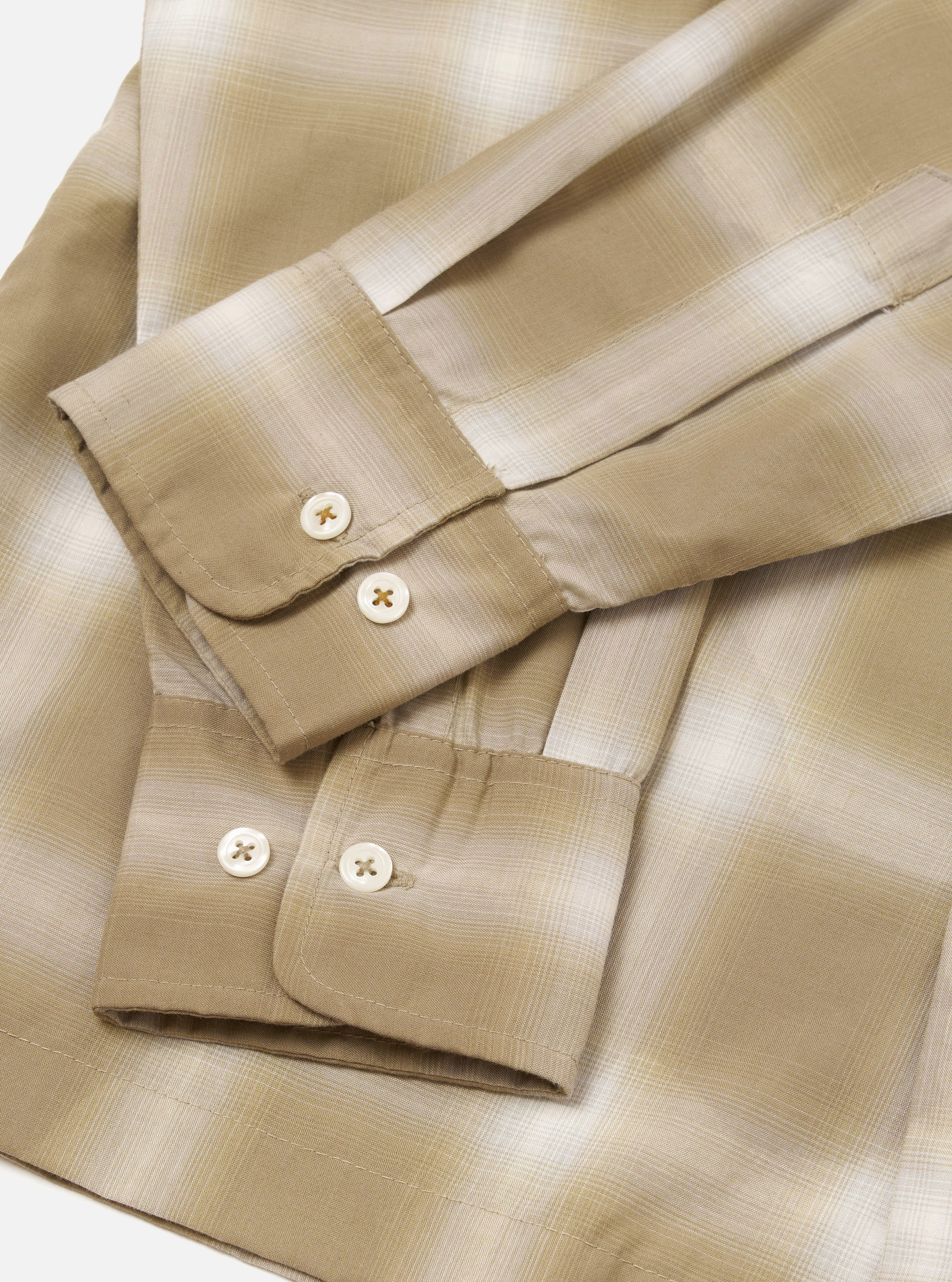 Flat lay close-up of the sand check shirt's cuffs and sleeves on a white surface. The fabric features a tonal ombre check pattern in beige, sand and cream. Both buttoned barrel cuffs are visible, each fastened with two cream four-hole buttons. The lightweight woven fabric has a subtle sheen.