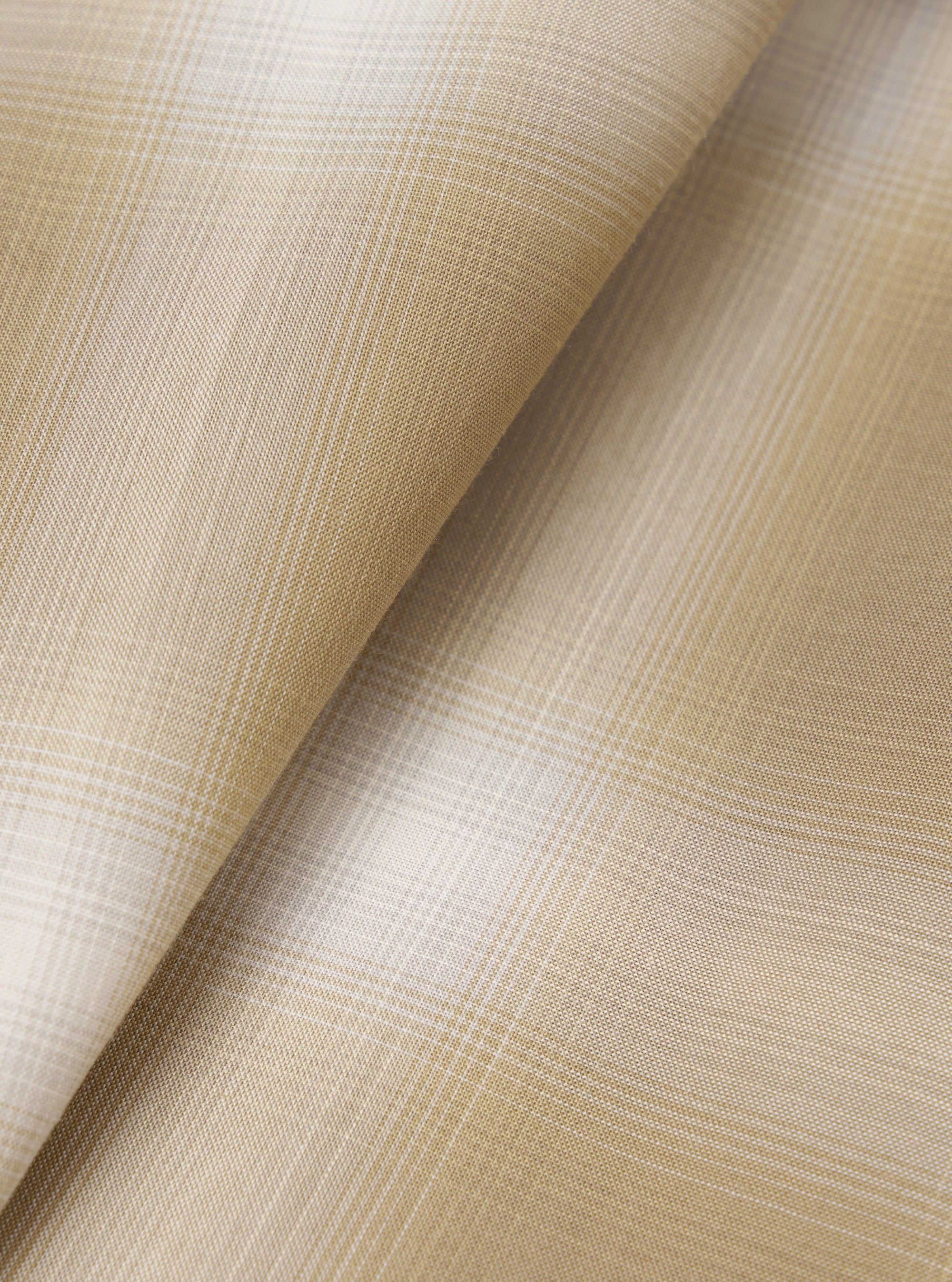 Close-up of the sand check fabric used in the Charlie Check Attendant Shirt, folded to show texture and pattern detail. A fine woven plaid in warm sand and white tones creates a subtle windowpane check across the lightweight, smooth fabric surface.