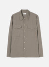 Sand and olive small-scale check long-sleeve shirt, flat lay on a light grey seamless backdrop. Pointed collar with a Universal Works woven label at the neck. Five cream buttons down the placket. Two patch pockets across the chest with visible topstitching detail along the edges and yoke seam. Plain cuffs, straight hem.