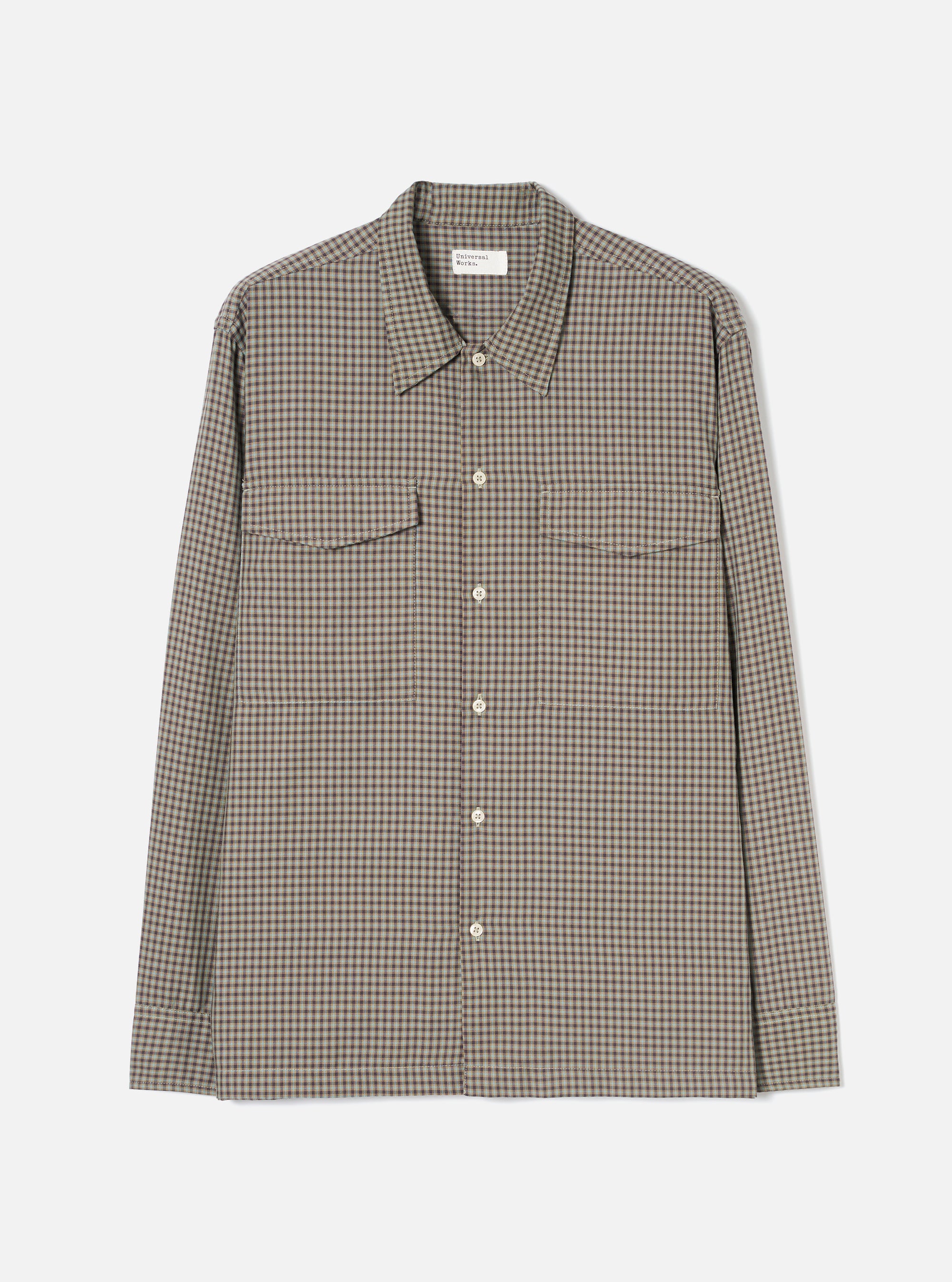 Sand and olive small-scale check long-sleeve shirt, flat lay on a light grey seamless backdrop. Pointed collar with a Universal Works woven label at the neck. Five cream buttons down the placket. Two patch pockets across the chest with visible topstitching detail along the edges and yoke seam. Plain cuffs, straight hem.