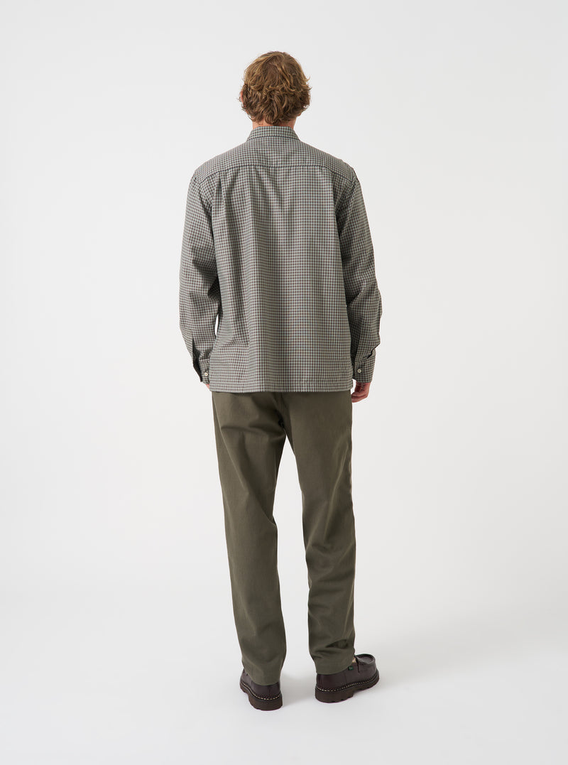 A back view of a model wearing the Universal Works Sand/Olive Parker Check Attendant Shirt. The image focuses on the back panel displaying the sand and olive check pattern, relaxed shoulder fit, and neat hem set against a plain backdrop.