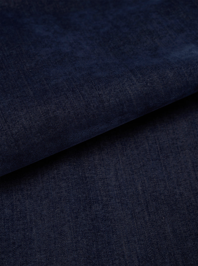 A close-up fabric swatch of the Navy Flock Chambray Warmus Jacket set against a plain neutral background, highlighting the deep navy blue tone, cotton weave texture, and subtle flock chambray finish of the material.