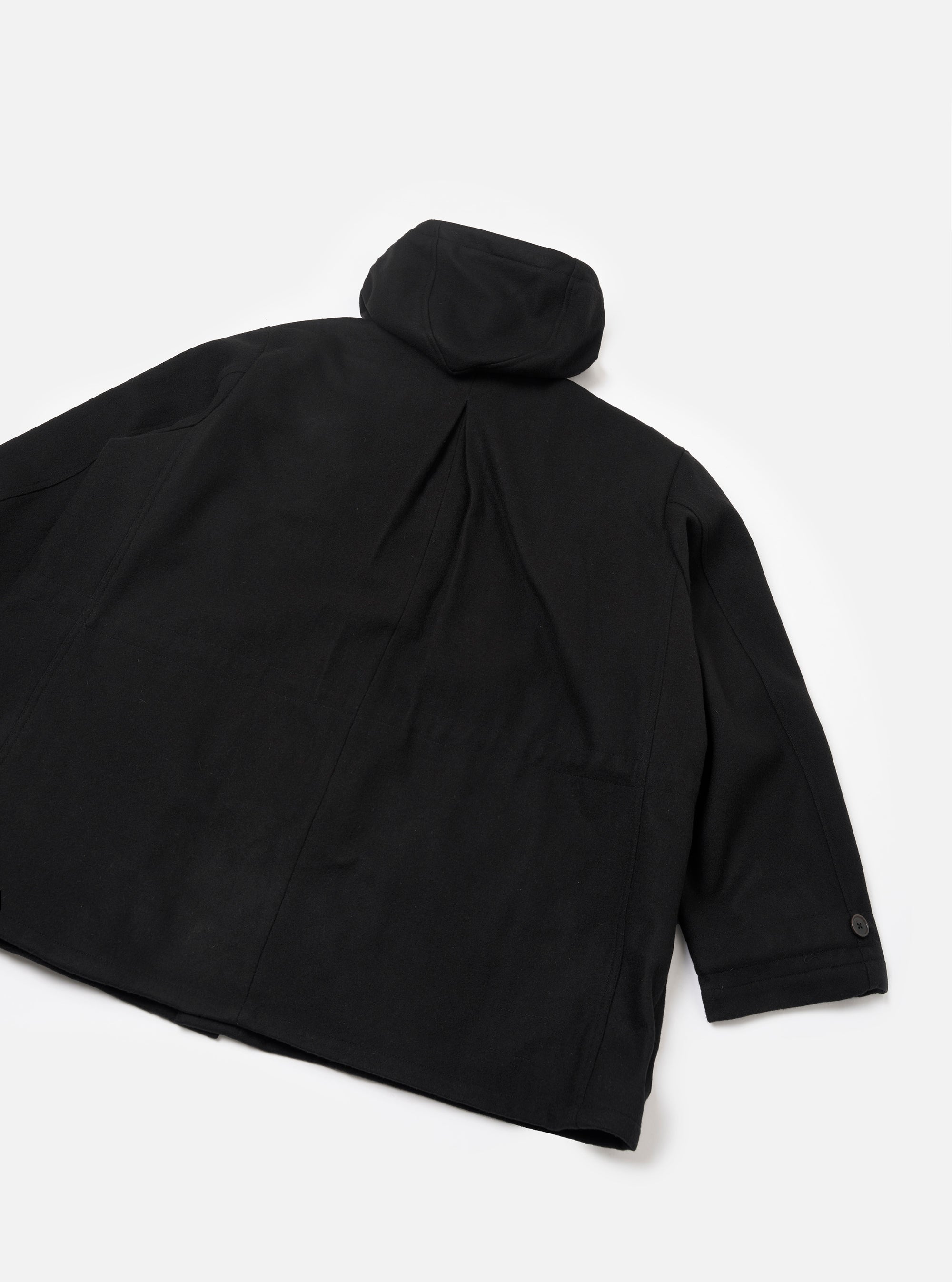 Black Mowbray Boston Parka laid flat on a white studio surface, showing the back. Smooth black fabric with curved seam detailing. A rolled hood sits at the collar. One sleeve is visible with a dark button at the cuff. Straight hem with a central back seam and slight drape.