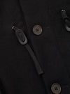 Close-up of the black Mowbray Boston Parka in a brushed wool-blend fabric. Two dark brown four-hole buttons are visible alongside toggle-and-loop duffle fastenings: braided black cord threaded through a metal ring and secured with a matte black oblong toggle. A patch pocket seam is visible at the top of the frame.
