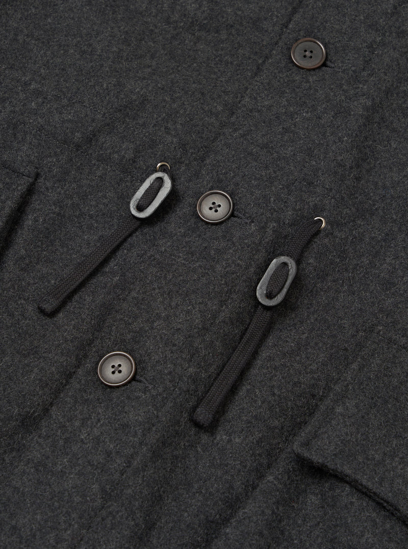 Close-up detail shot of the grey marl wool-blend fabric on the Mowbray Boston Parka. Three dark horn-effect four-hole buttons are visible alongside two black woven toggle loops with metal hooks, forming the double-breasted fastening. A welt pocket edge is visible to the left.