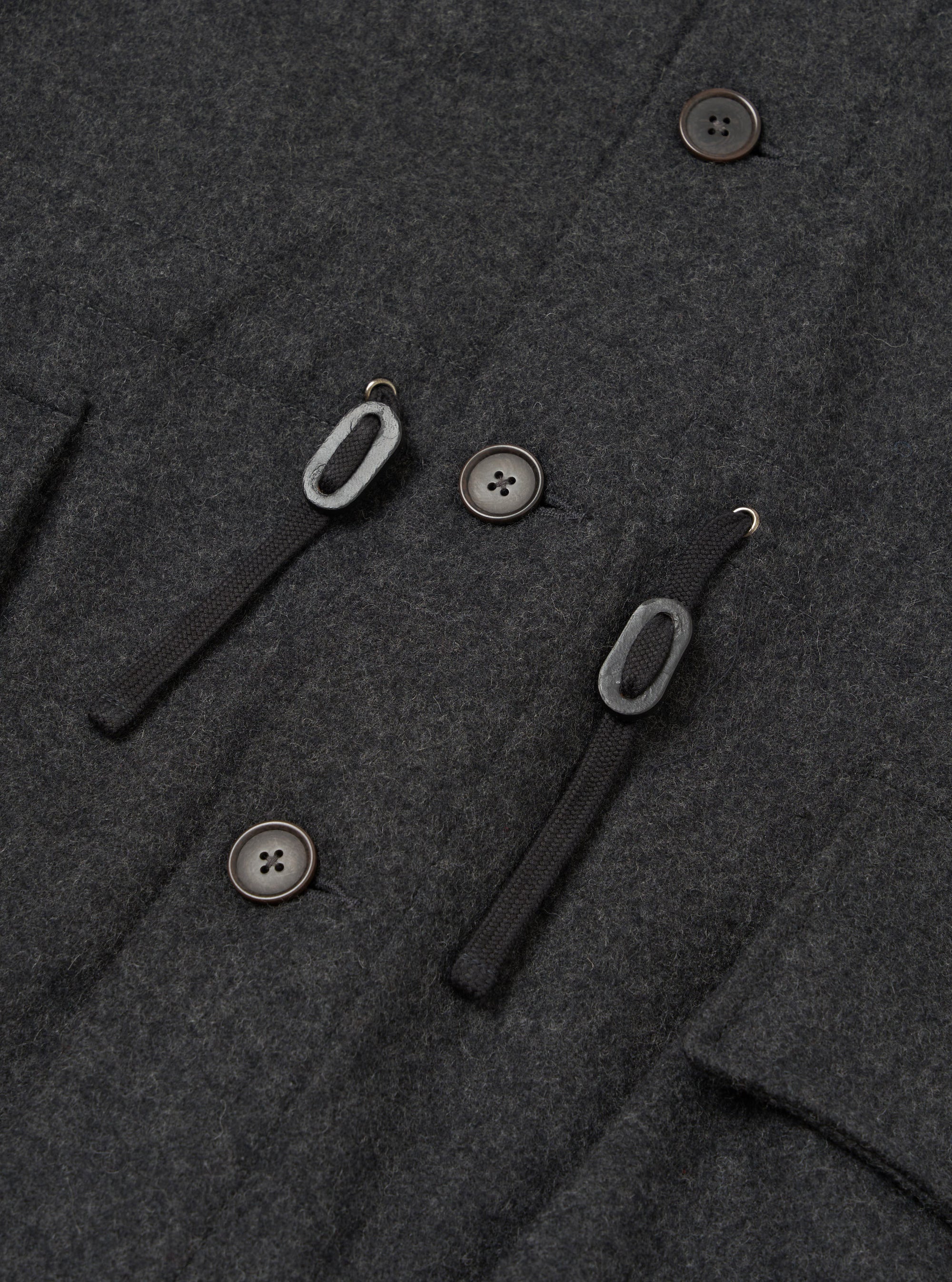 Close-up detail shot of the grey marl wool-blend fabric on the Mowbray Boston Parka. Three dark horn-effect four-hole buttons are visible alongside two black woven toggle loops with metal hooks, forming the double-breasted fastening. A welt pocket edge is visible to the left.