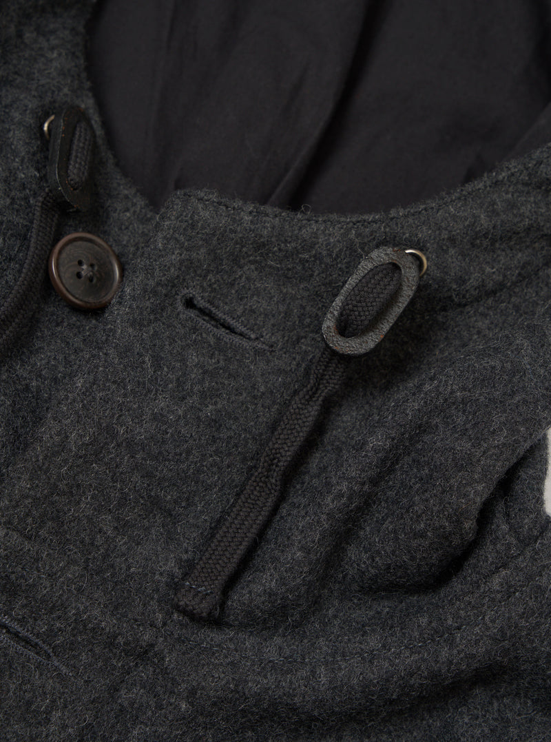 Close-up of the grey marl wool-texture parka's hood and collar area. A dark brown four-hole button fastens the hood toggle loop on the left. A braided drawcord threads through a metal eyelet on the right. The hood's dark navy lining is visible behind the collar. Shot on a plain light grey seamless backdrop.