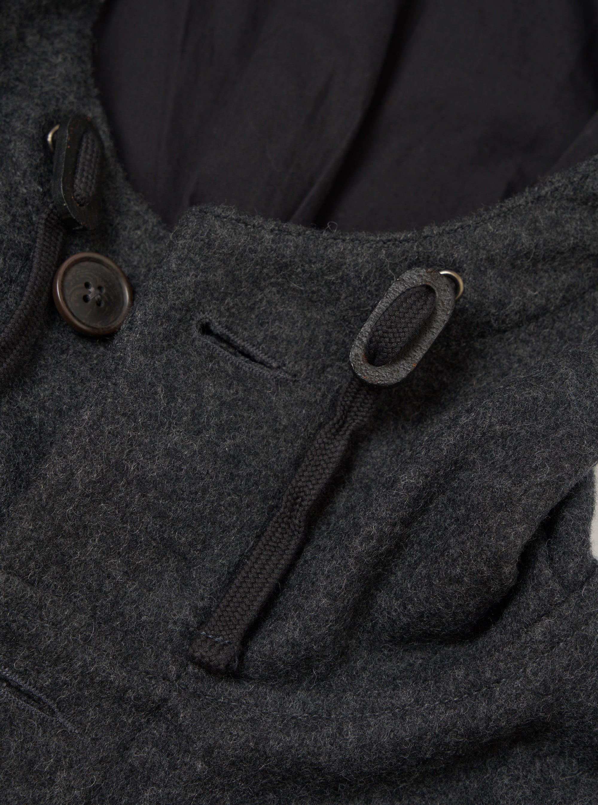 Close-up of the grey marl wool-texture parka's hood and collar area. A dark brown four-hole button fastens the hood toggle loop on the left. A braided drawcord threads through a metal eyelet on the right. The hood's dark navy lining is visible behind the collar. Shot on a plain light grey seamless backdrop.