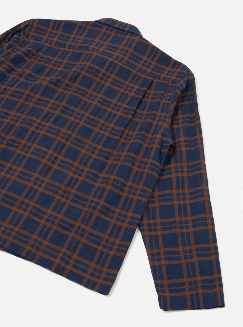 A studio back view of the Navy/Brown Young Check Zip Shirt set against a white backdrop. The image showcases the straight hem, clean shoulder yoke, and subtle navy blue and brown check grid woven into the cotton fabric.