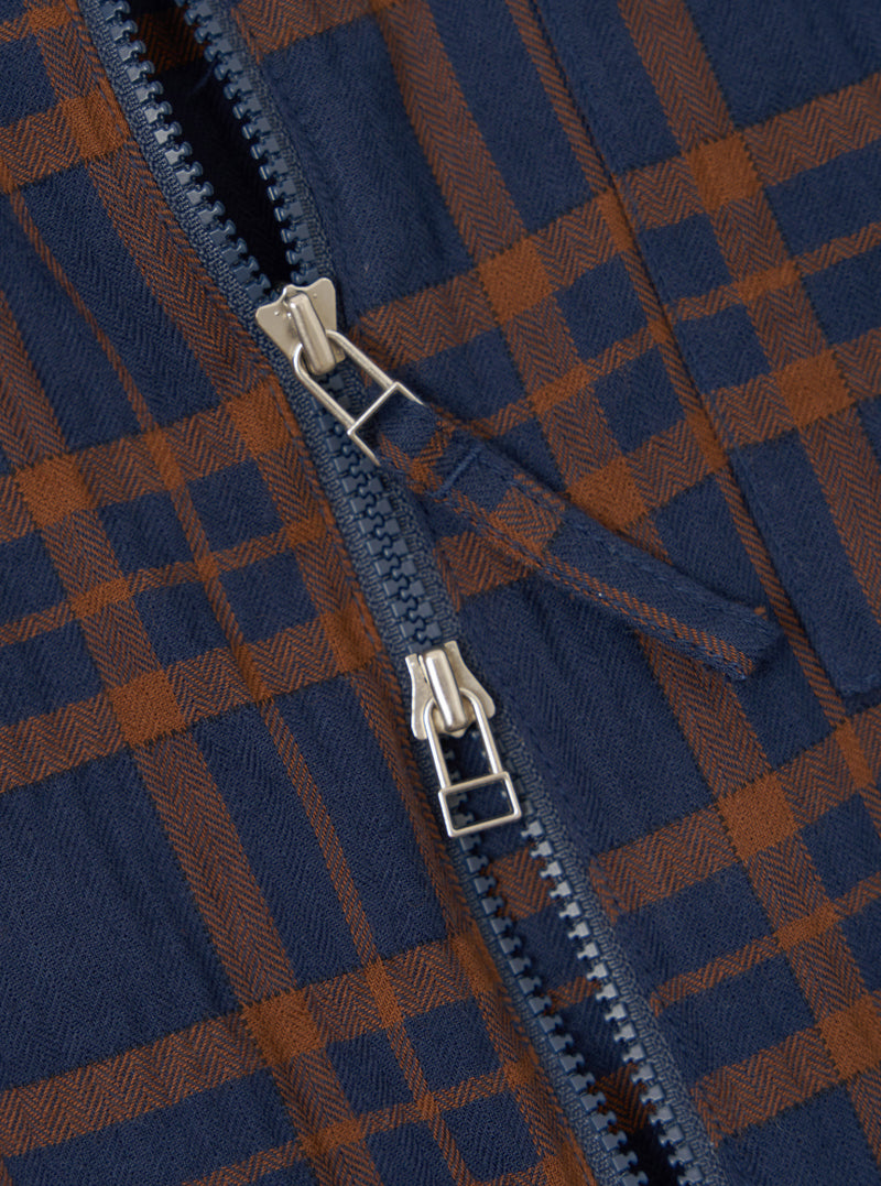 A close-up detail shot of the upper portion of the Navy/Brown Young Check Zip Shirt on a plain background. The image highlights the metallic zip puller, pointed collar construction, and textured navy and brown check cotton fabric.